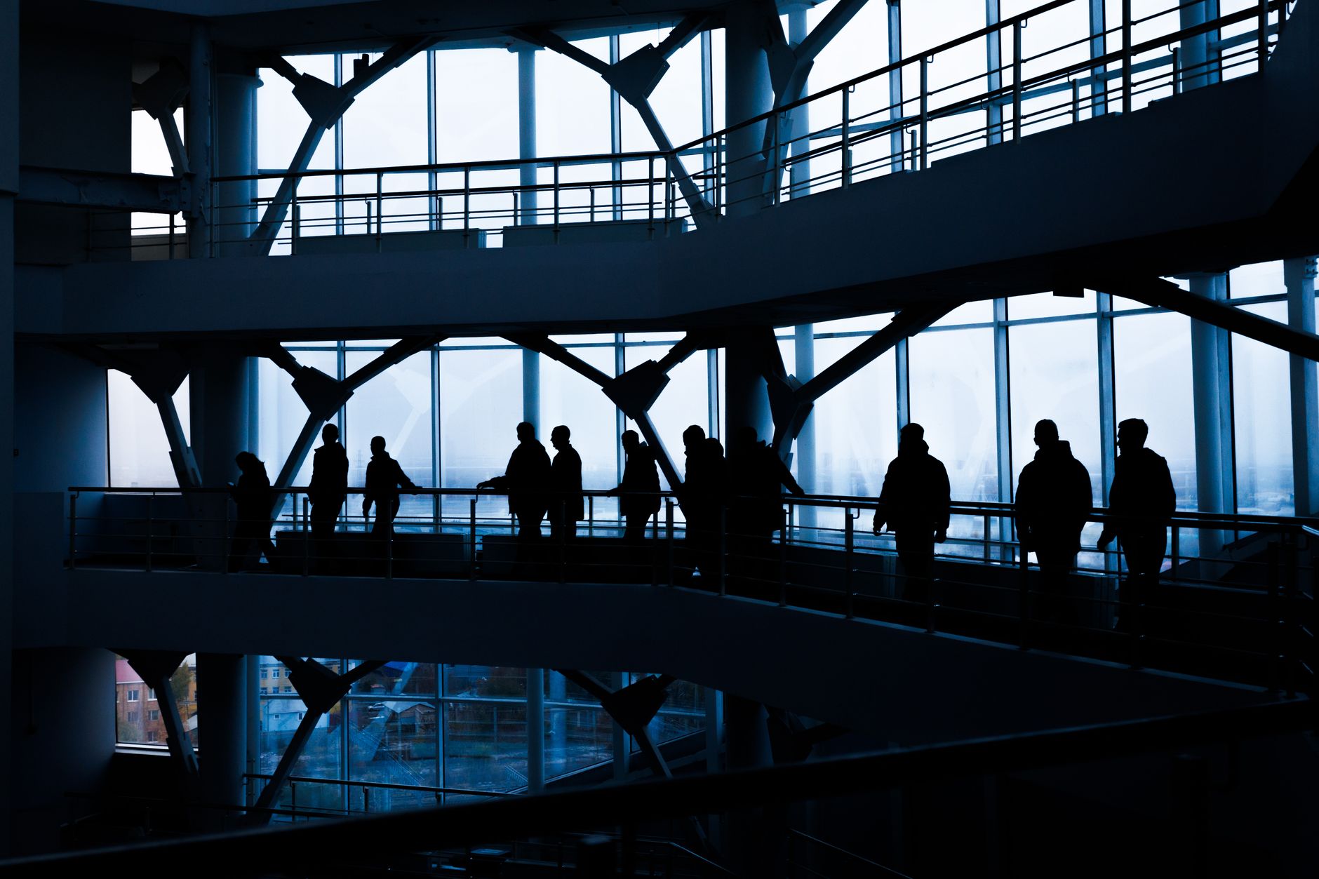 Silhouettes of people walking in a modern architectural building with large windows. — A Legacy of Rebuilding: Arman Gabaee P