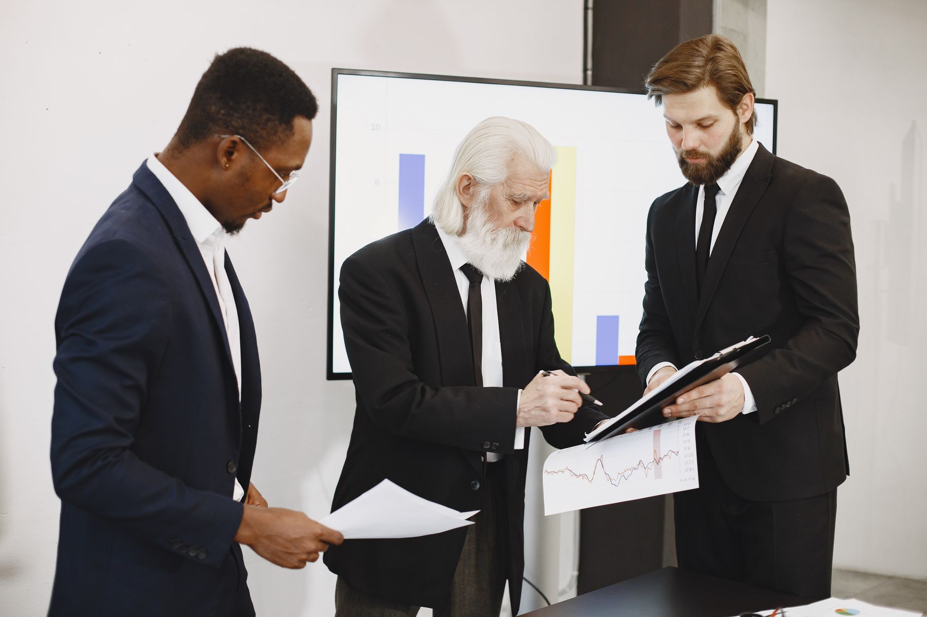 Three businessmen in suits reviewing reports and graphs during an office meeting. — Affordable Window Replacement Sanford Hom