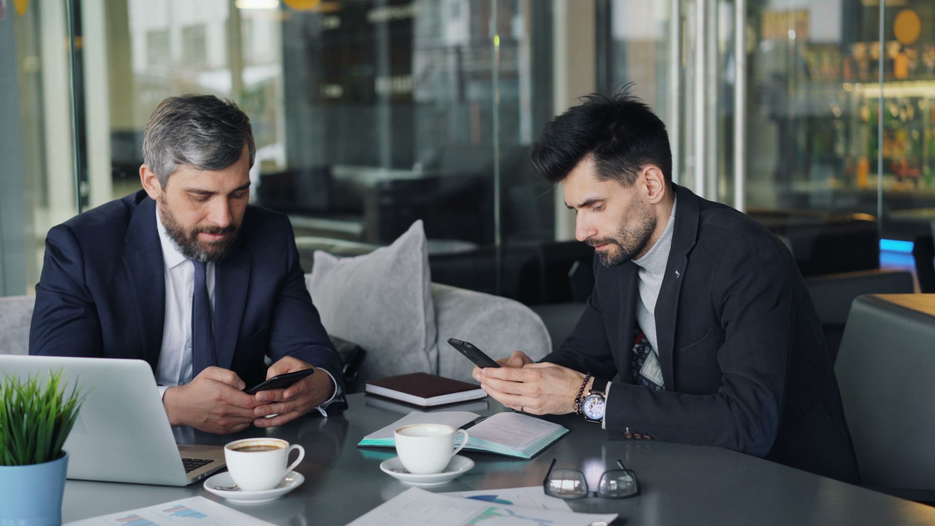 Two businessmen in a cafe working on smartphones and laptops, engaged in a meeting. — Buy Weed Online Canada From a Trusted a