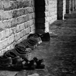 A row of various shoes lined up against a textured brick wall in black and white