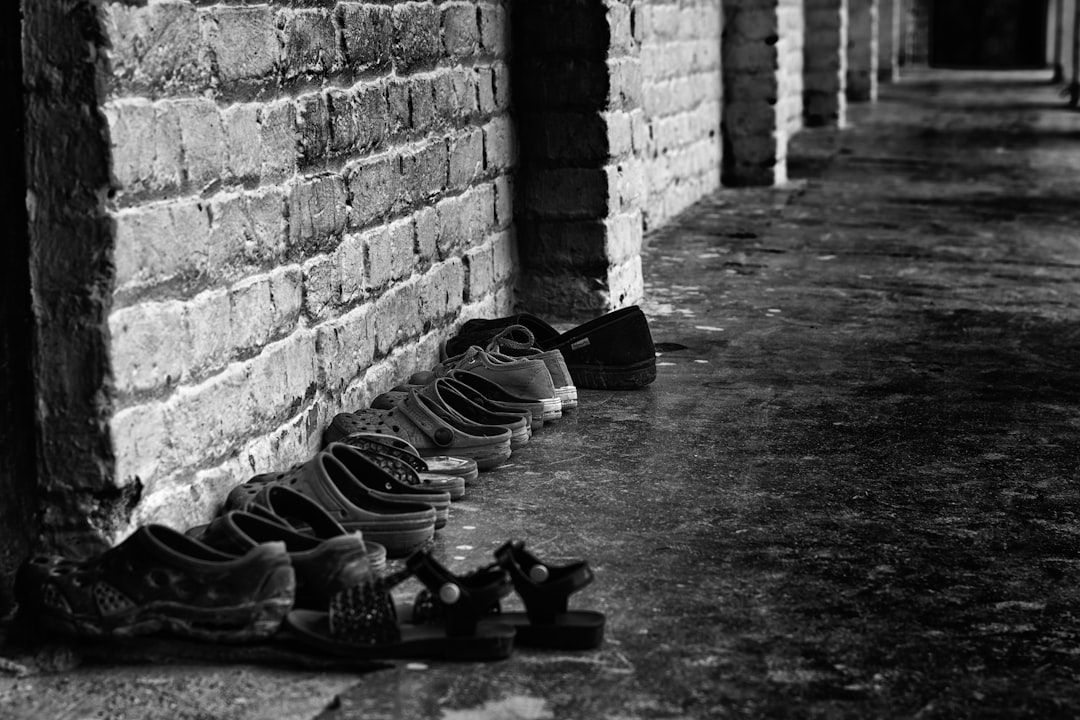 A row of various shoes lined up against a textured brick wall in black and white