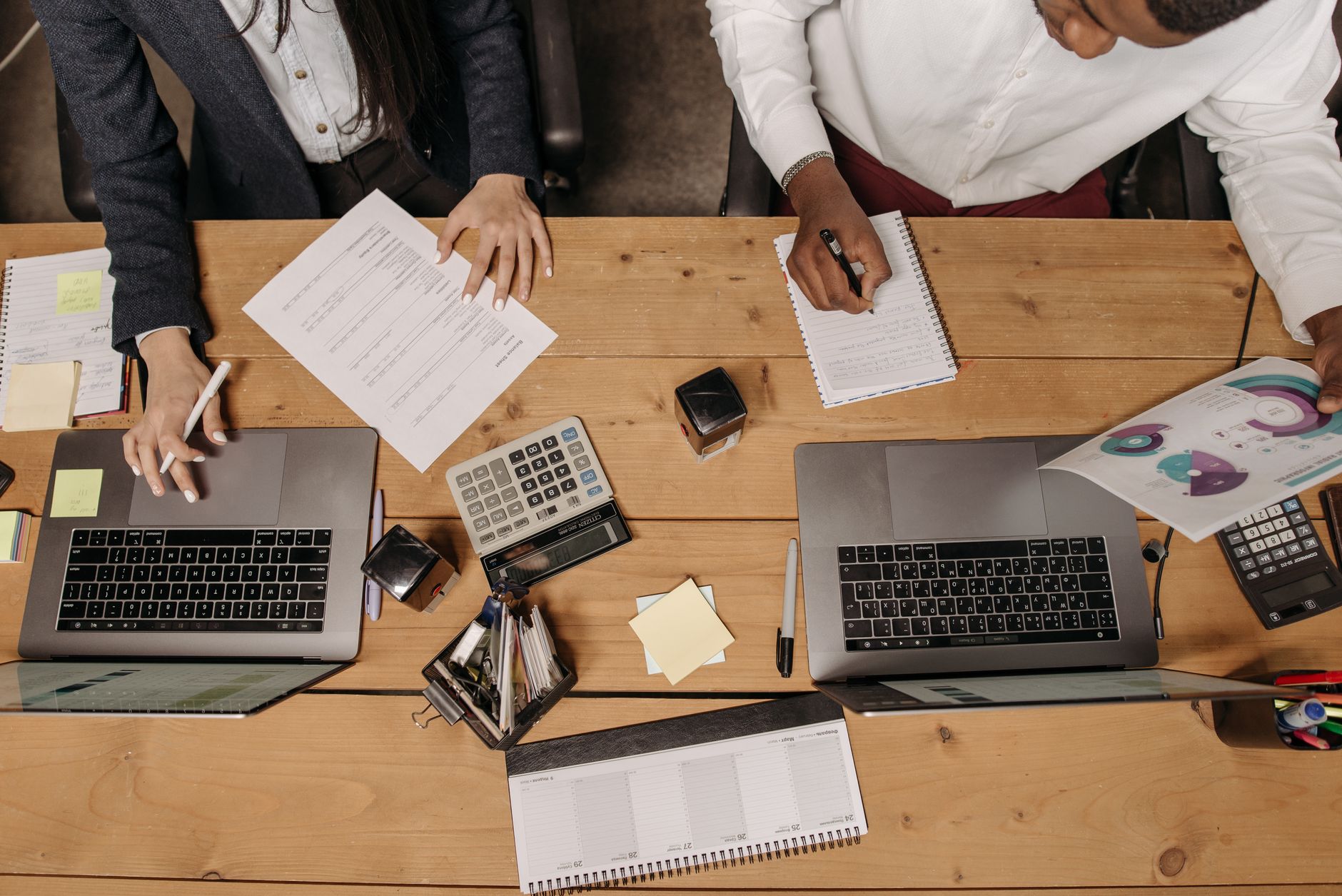 High-angle view of professionals working collaboratively with laptops and documents in an office. — Dr. Zachary Lipman Bridge