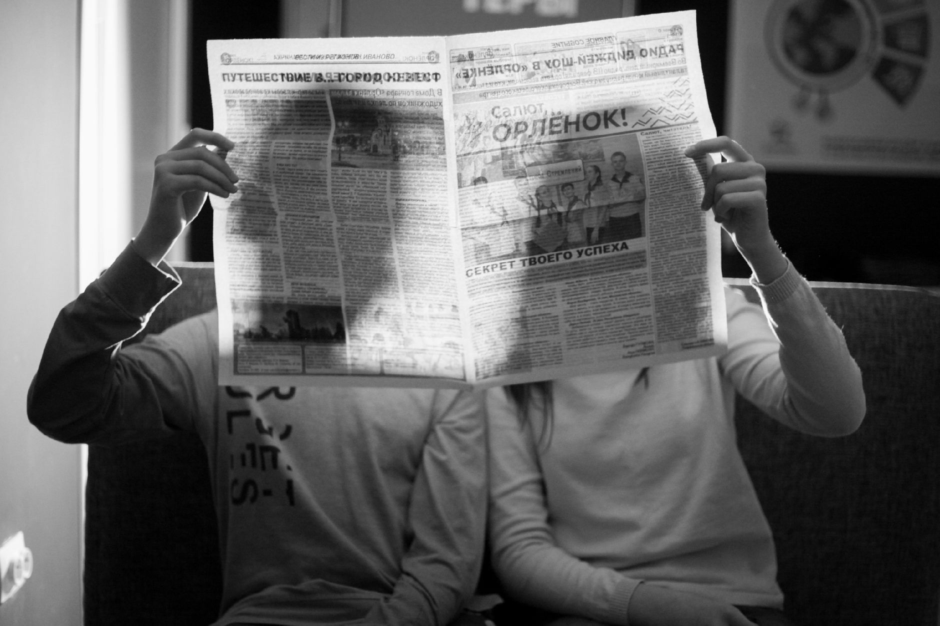 A couple sitting indoors reading a newspaper in a black and white photograph. — Enhance Betting Awareness Through Live Toto B