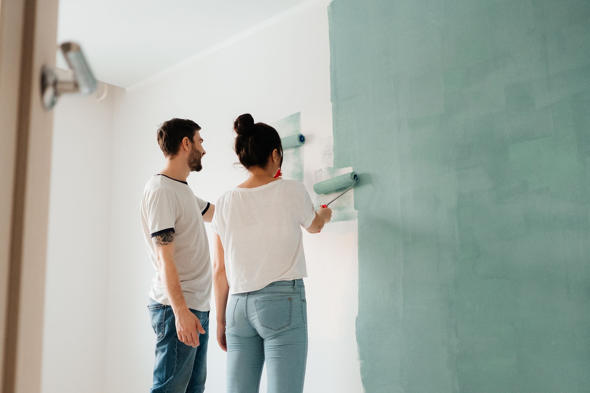 A couple collaborates to paint a wall with a roller indoors, showcasing teamwork. — "Expert Window Replacement in Bellevue fo
