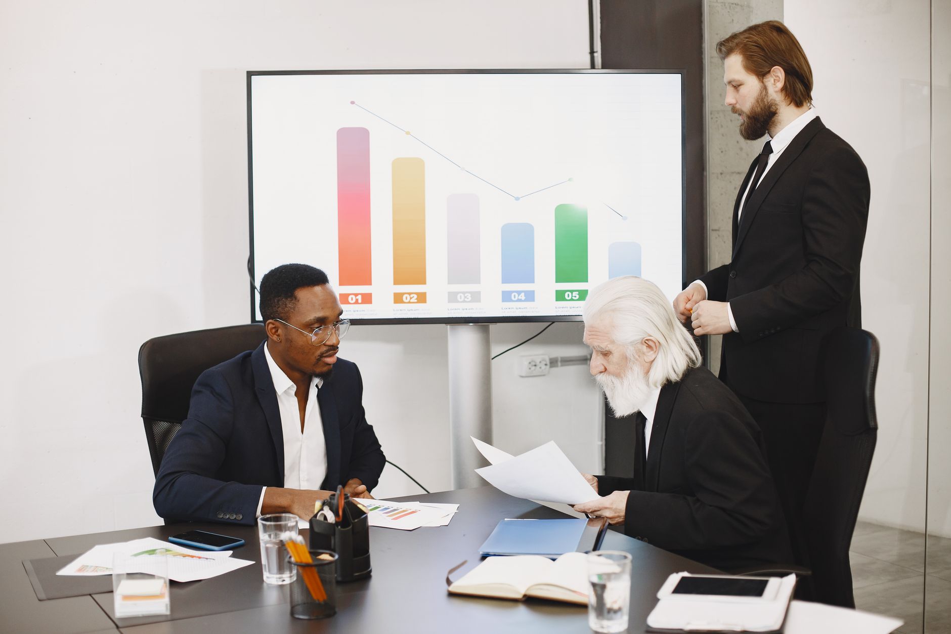 Three businessmen discussing financial data in a modern office setting with charts. — Success Stories of Leading Korean Digit